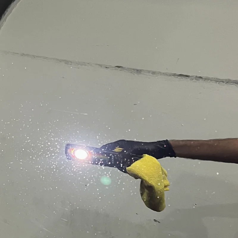 The same black panel under the same inspection light after machine polishing, with the swirl marks gone