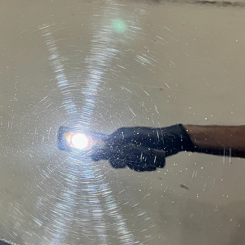 Swirl marks and fine scratches revealed across black paint by a handheld inspection light, before machine polishing