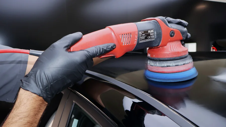 A large machine polisher cutting the paint on a black panel during paint correction