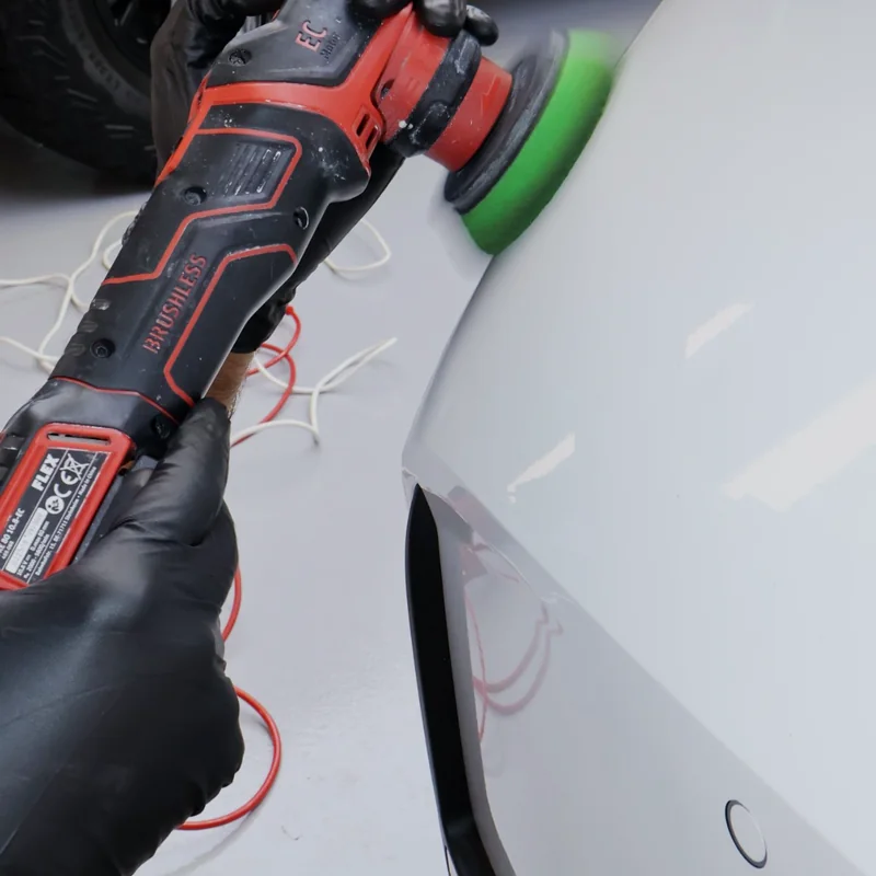 Close-up of a dual-action polisher working the rear quarter of a white car