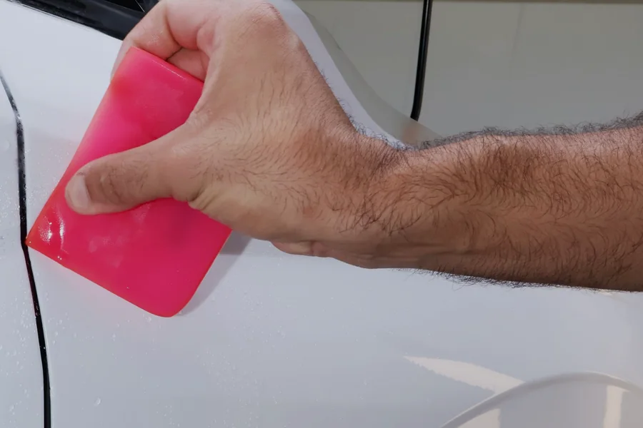 Protective film being squeegeed along the panel edge of a white car