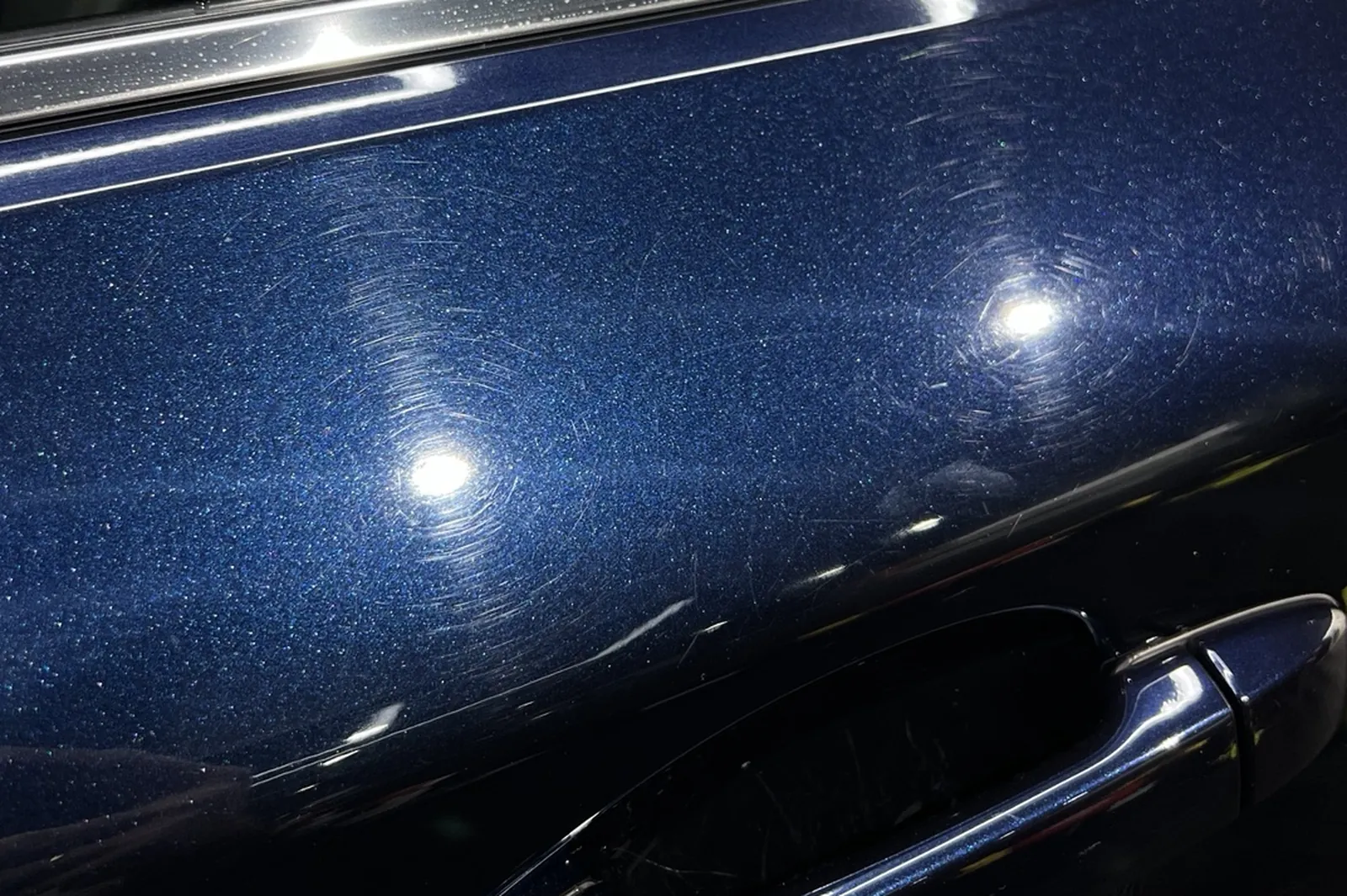 The same blue Subaru door before polishing — circular swirl marks and wash marring across the panel