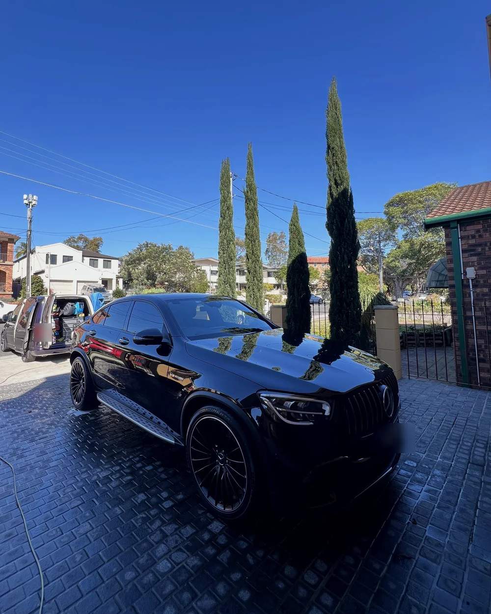 Need for Studio van parked at a customer's home beside a freshly washed black Mercedes-AMG GLC in the driveway